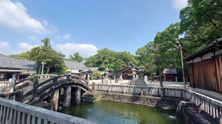 池に架かる石の太鼓橋と木々に囲まれた神社の境内